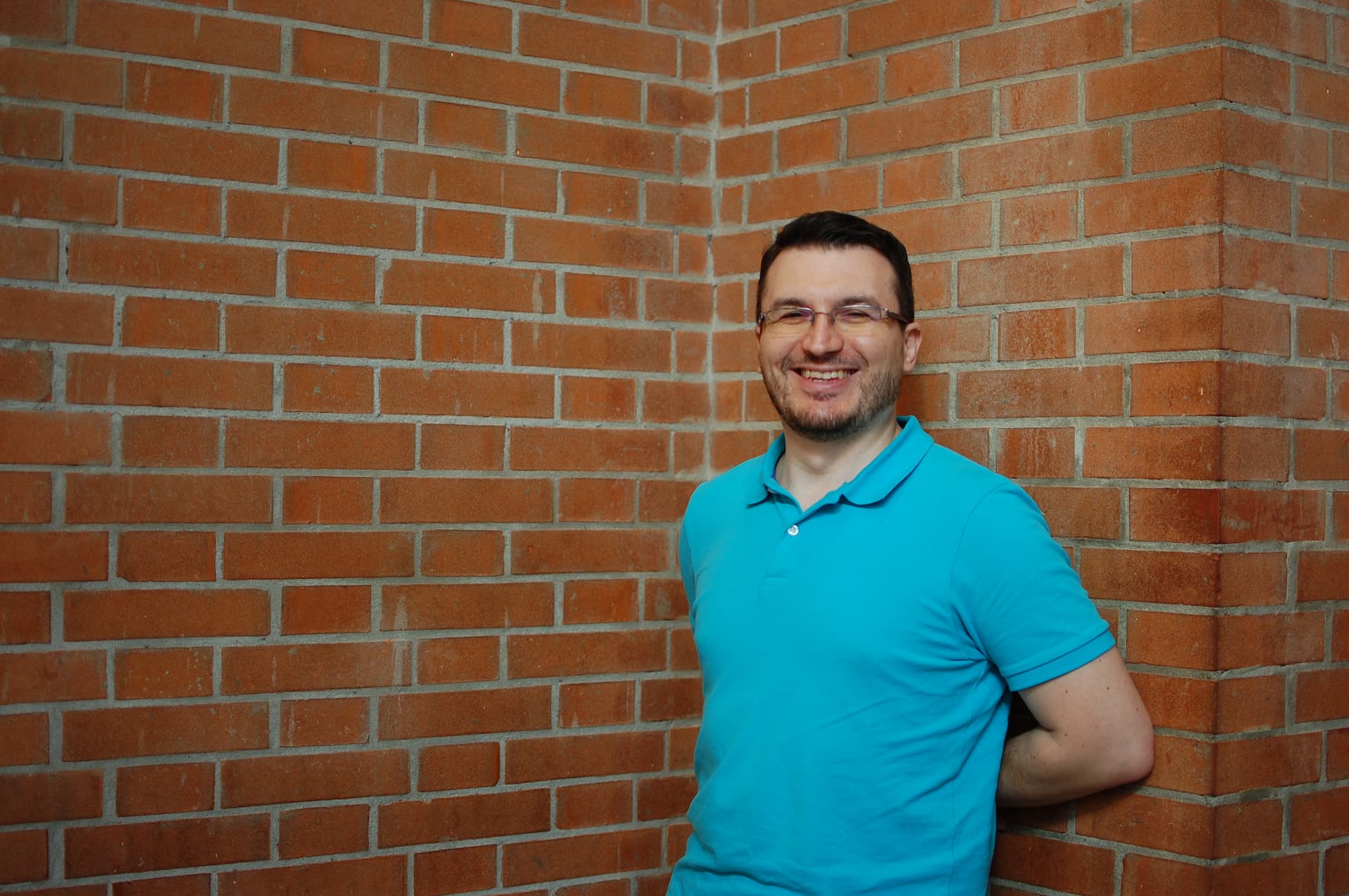 Matteo Greco smiling at the camera in front of a brick wall